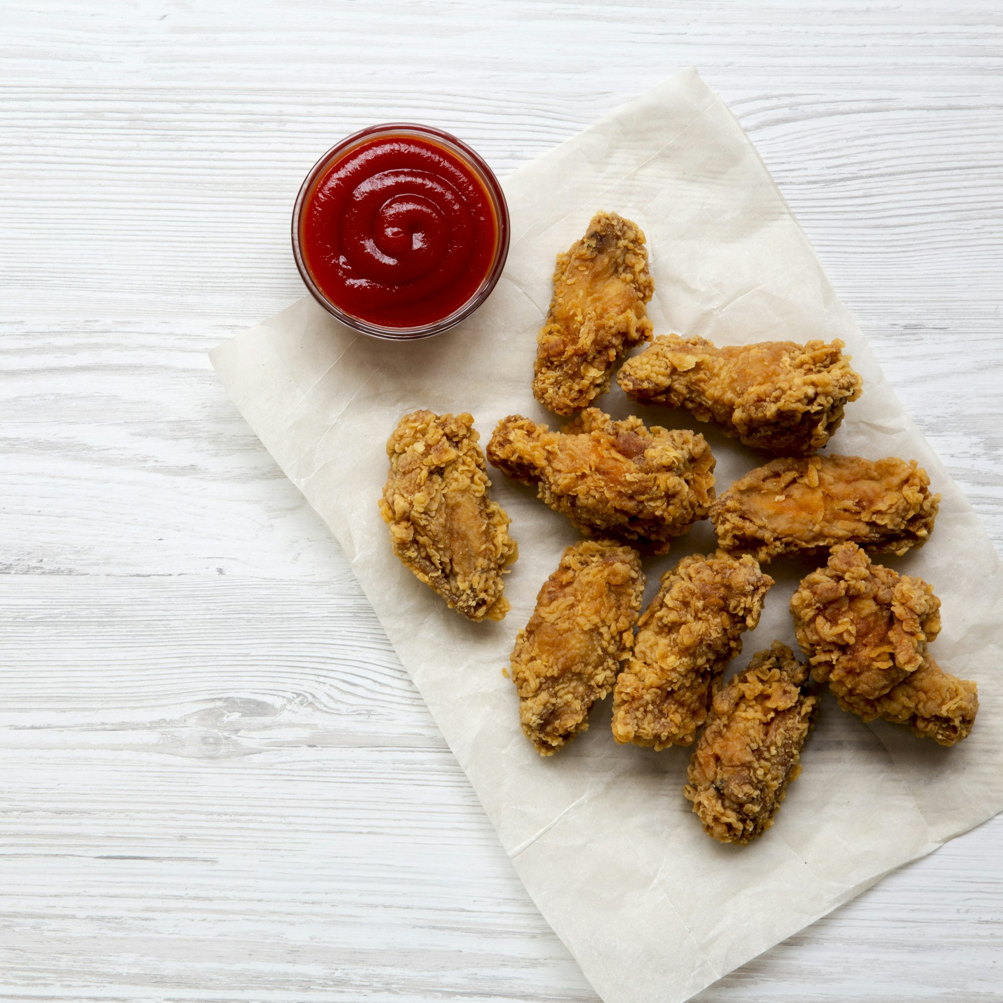 Fried chicken wings with ketchup on a white wooden background, overhead view.